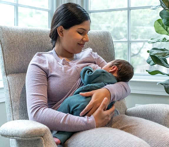 Mom seated comfortably on couch holding baby in a cradle hold