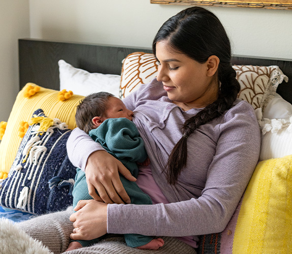 Mom sitting on sofa in semi-reclined position with baby positioned entirely on mother